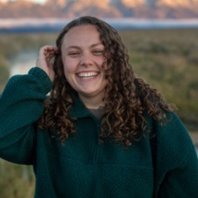 Person smiling in nature with mountains in the background.